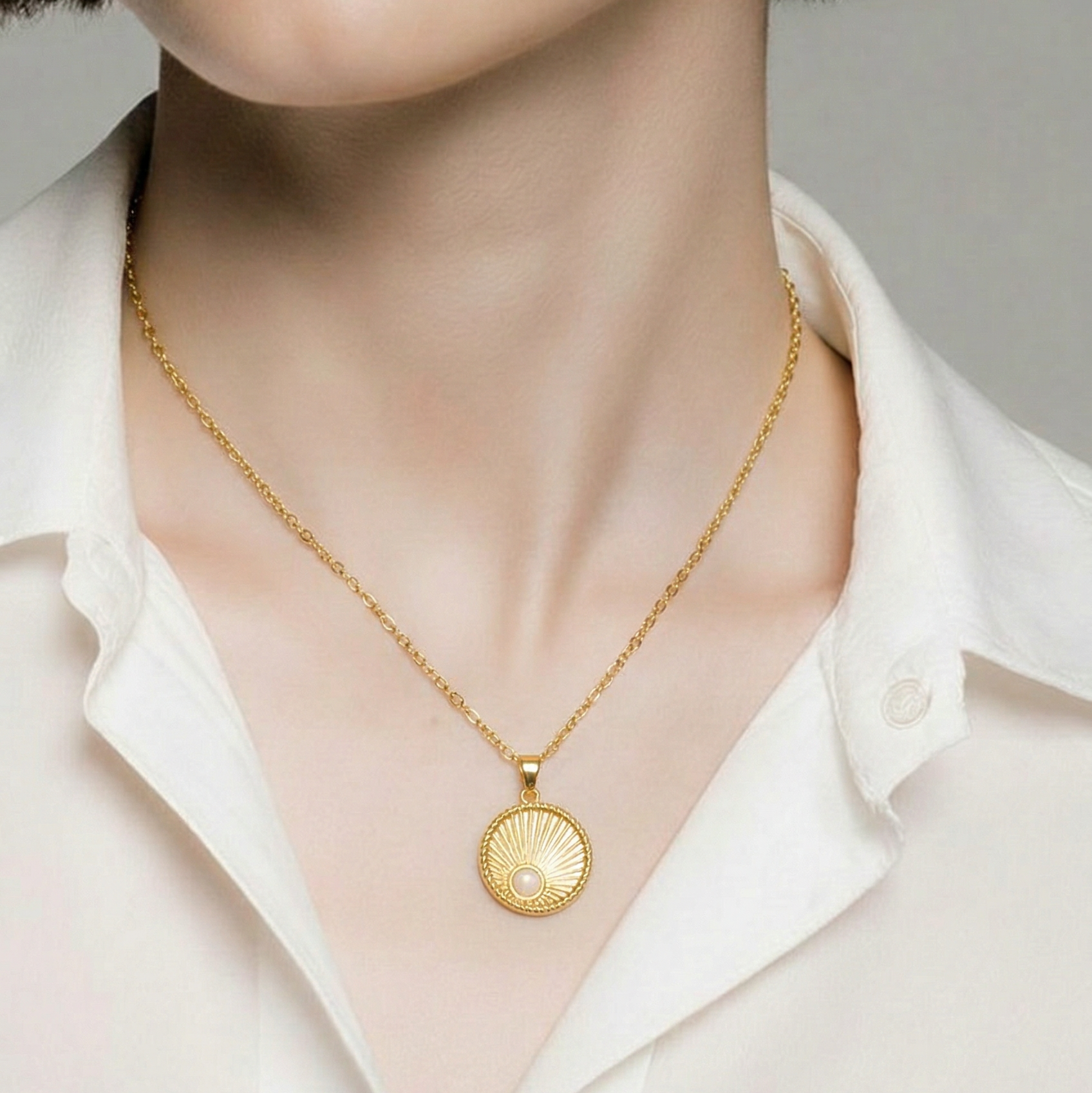 Close-up of a person wearing a textured round gold pendant necklace on a plain background